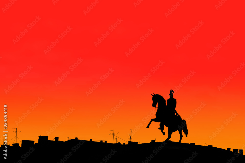 Monument to Tsar Nicholas I in St. Petersburg in Russia on St. Isaac's Square. Silhouette of a monument and a house under it on a red and orange background at sunrise. Copy space for text