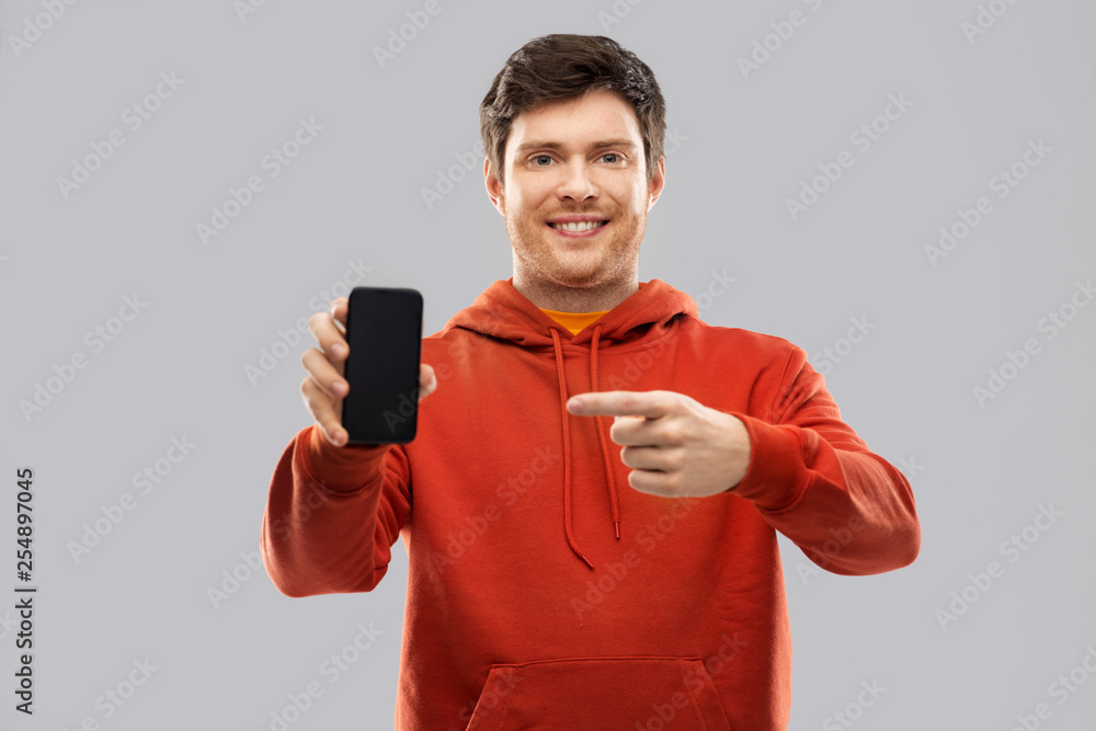 technology and people concept - smiling young man in red hoodie showing black smartphone with blank screen over grey background technology and people concept - smiling young man in red hoodie showing black smartphone with blank screen over grey background