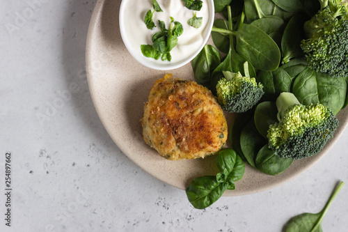 Delicious fried meat cutlets. Chicken or turkey cutlets with carrot and spinach served with broccoli, spinach and sour cream sauce. Light grey concrete background.