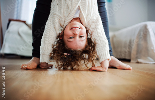 An unrecognizable mother holding small girl upside down at home.