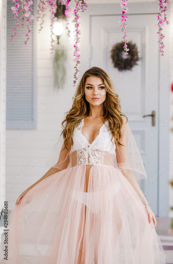 Fototapeta premium Cute girl in soft pink negligee poses in a spring studio