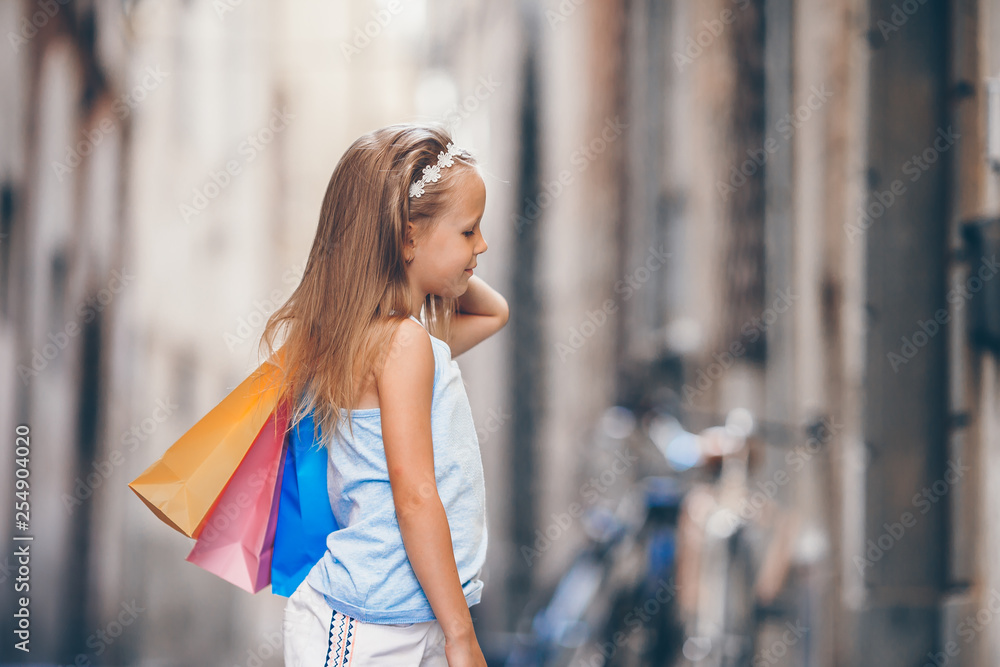 Portrait of adorable little girl walking with shopping bags outdoors in european city.