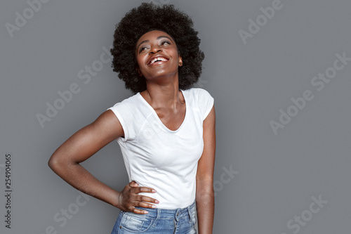 Young woman standing isolated on gray posing hand on hips smiling cheerful