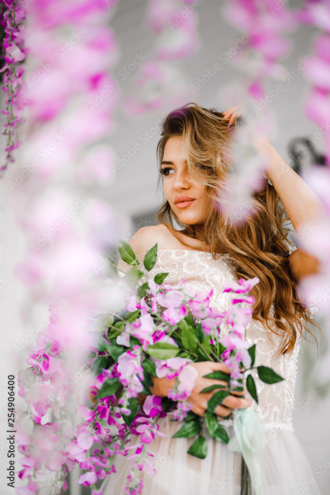 Naklejka premium Comely woman in a white dress standing with pink flowers in her arms