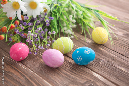 Colorful Easter eggs and spring flowers on rustic wooden background.