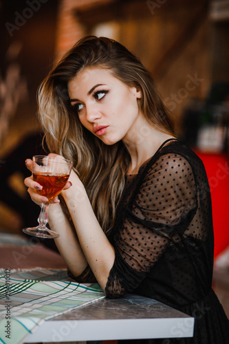 A sexy blonde holds a glass of cognac in her hand