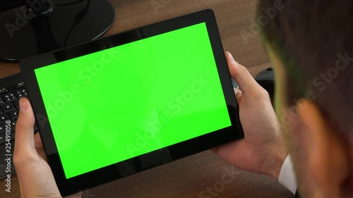 An office worker looks at a tablet with a green screen at a desk with a computer - closeup