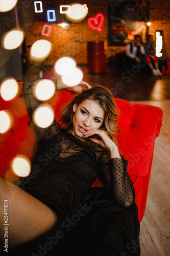 A glowing girl in a black dress lays on the red sofa