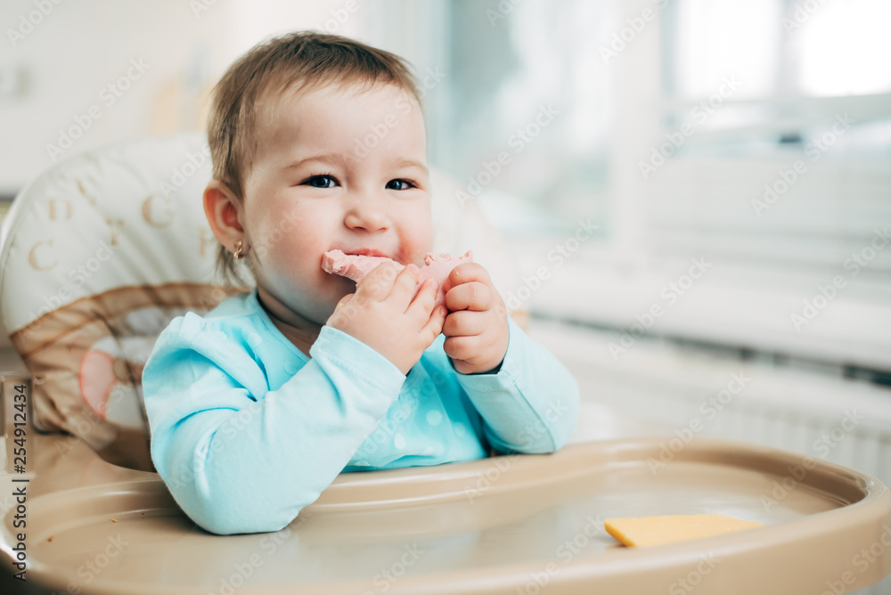 a little girl in a high chair eating a piece of boiled sausage a little girl in a high chair eating a piece of boiled sausage