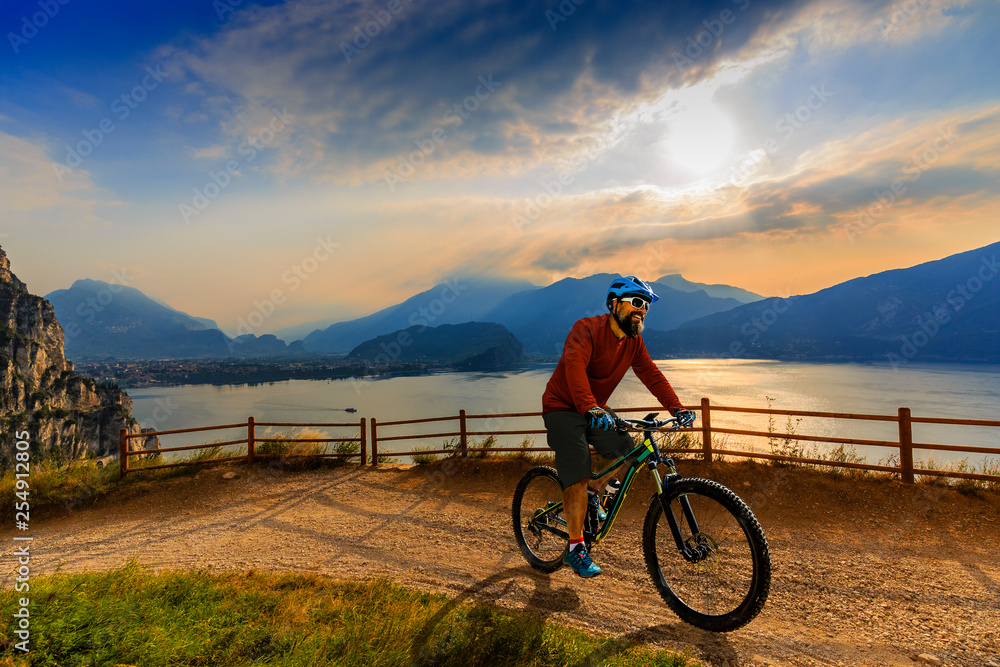 Cycling man riding on bike at sunrise mountains and Garda lake landscape. Cycling MTB enduro flow sentiero ponale trail track. Outdoor sport activity.
