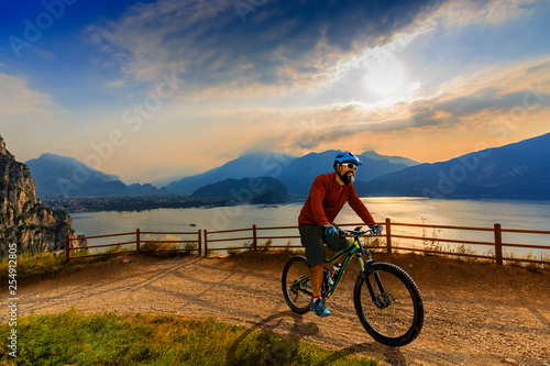 Fototapeta Naklejka Na Ścianę i Meble -  Cycling man riding on bike at sunrise mountains and Garda lake landscape. Cycling MTB enduro flow sentiero ponale trail track. Outdoor sport activity.