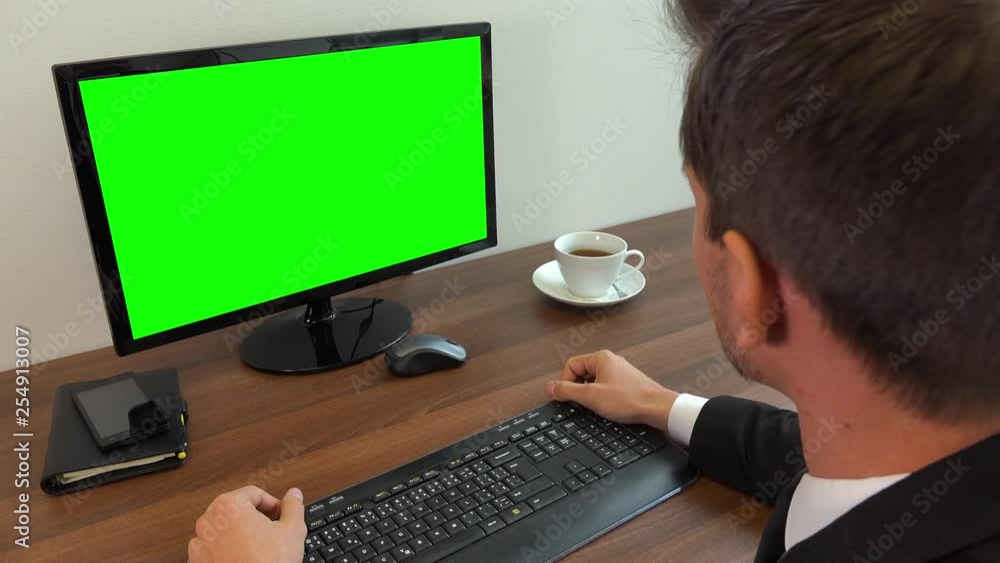 An office worker in a suit sits at a desk with a computer with a green screen and acts angry - closeup An office worker in a suit sits at a desk with a computer with a green screen and acts angry - closeup