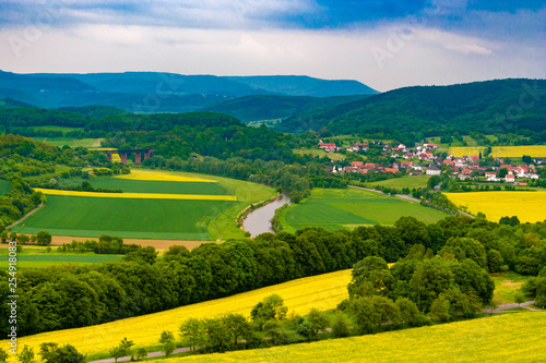 Fototapeta Naklejka Na Ścianę i Meble -  A great landscape view of the Werra Valley with the river Werra, cultivated fields, a railway bridge and the town Oberrieden; surrounded by forest and the low-mountain range of Hesse and Thuringia.