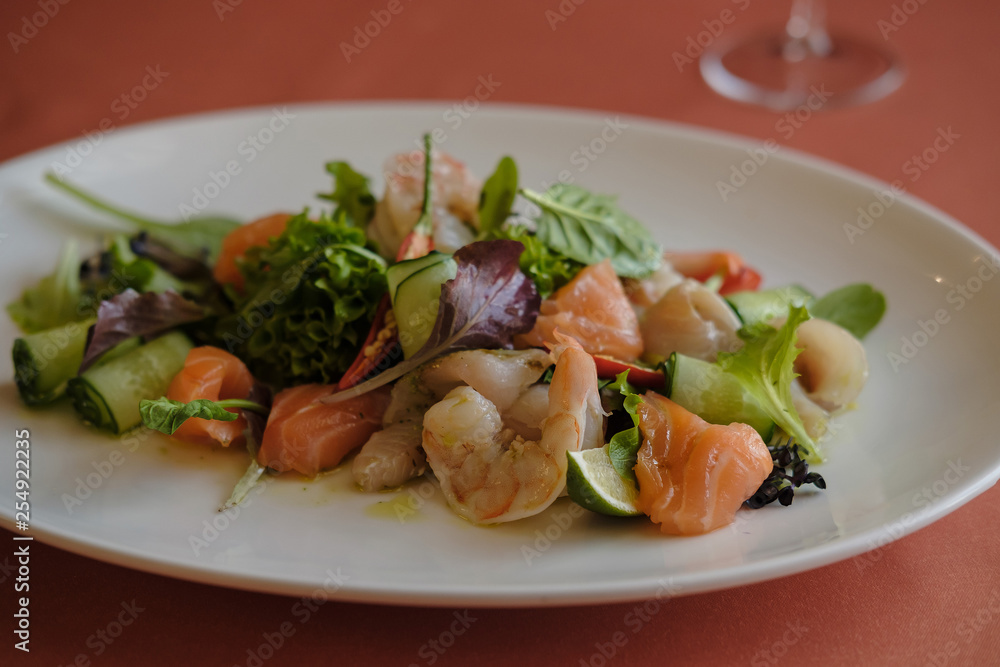 Fresh delicatessen salmon salad (trout) with lettuce, basil, pepper, prawn and cucumber with mustard dressing and olive oil in a white plate. Selective focus Fresh delicatessen salmon salad (trout) with lettuce, basil, pepper, prawn and cucumber with mustard dressing and olive oil in a white plate. Selective focus