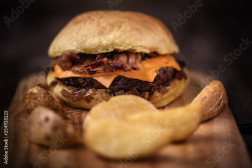 Homemade bacon burger and fried potato chips on wooden tray.