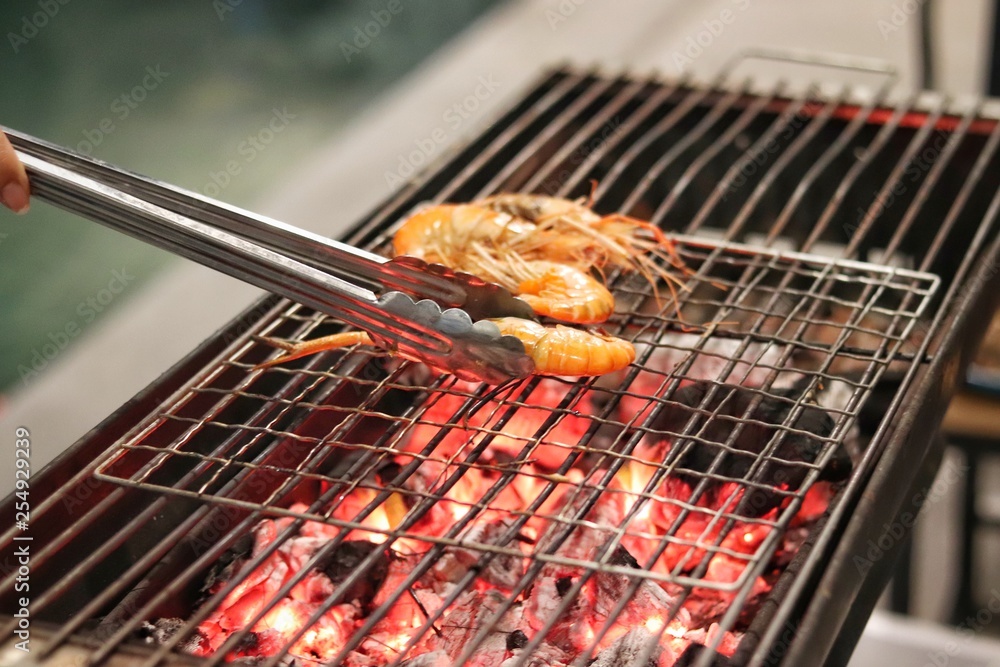 fresh shrimp is grilled on a charcoal stove in night with a party.