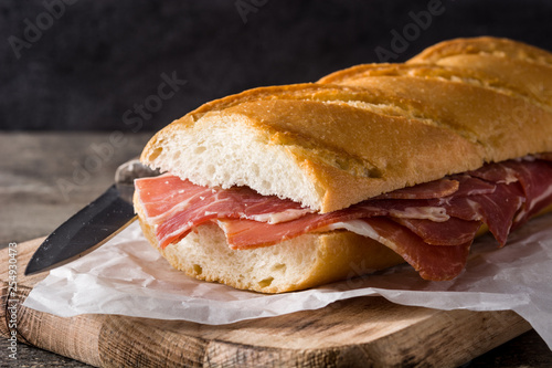 Spanish serrano ham sandwich on wooden table.