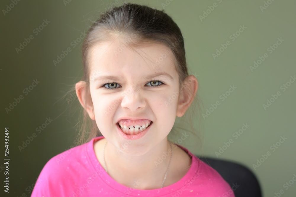 Green eyed caucasian white girl with fun angry face and pink t-shirt on blurred neutral background. Kid emotional portrait. Funny expression faces. Green eyed caucasian white girl with fun angry face and pink t-shirt on blurred neutral background. Kid emotional portrait. Funny expression faces.
