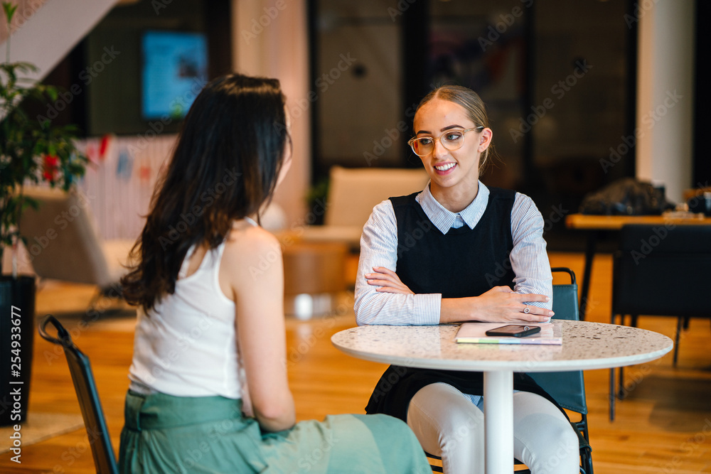Fototapeta premium Two magnificent ladies discussing a record inside a bistro. They are talking about certain exercises while sitting on a table.