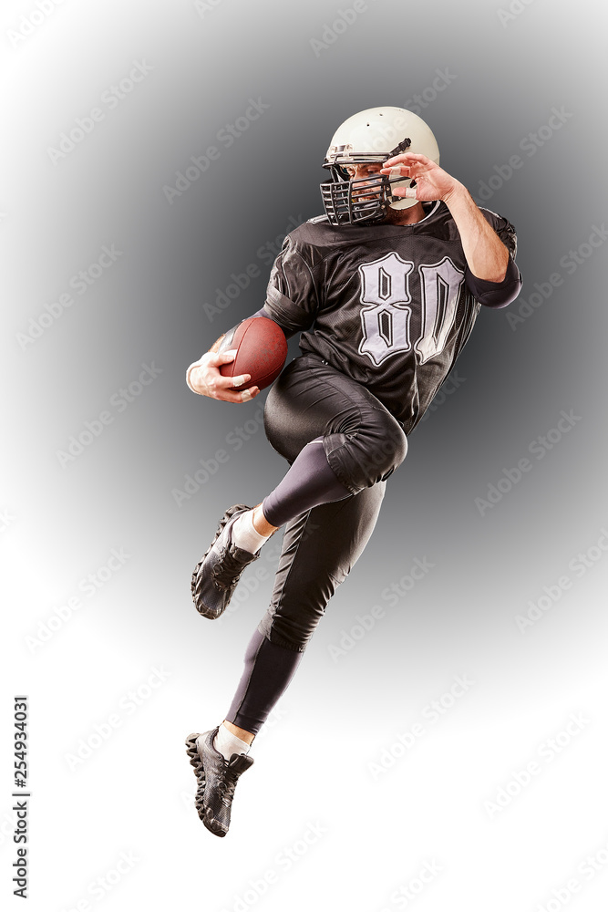 american football player in dark uniform jumping with ball on gray background
