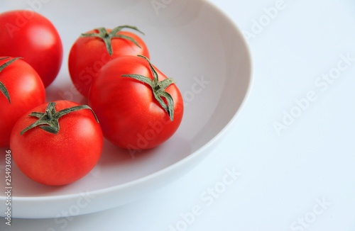 red tomatoes in a white plate on a white background © Julia