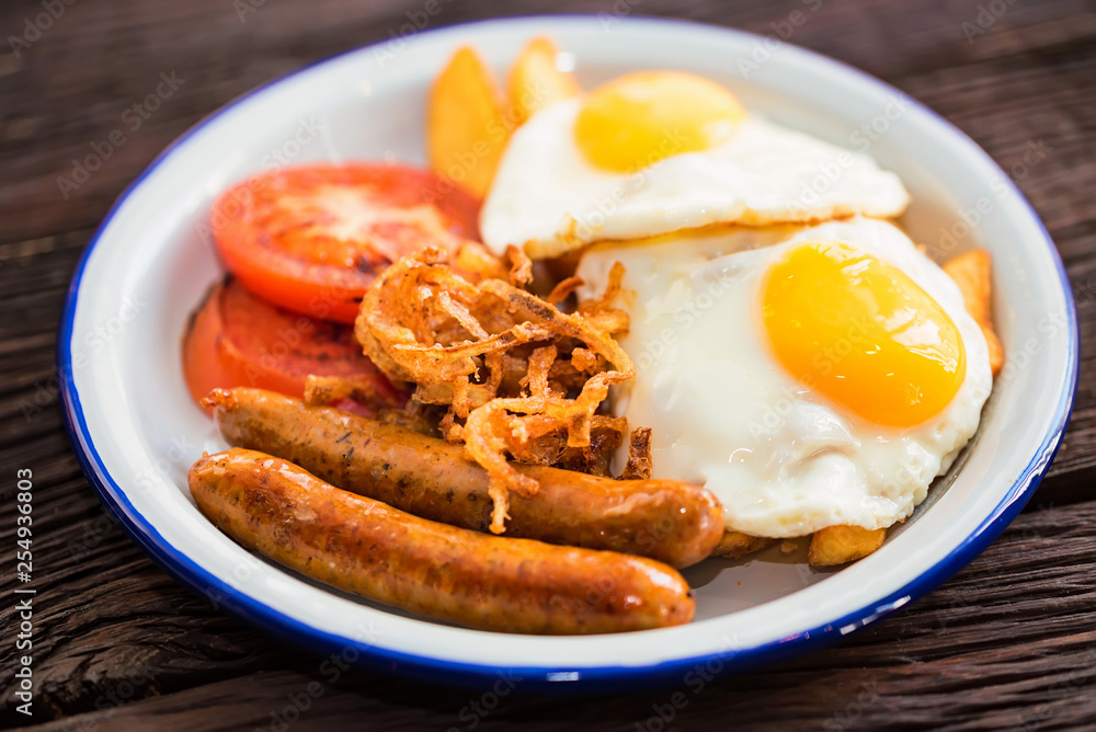 Typial breakfast with eggs, tomato, onion rings and sausage on plate Typial breakfast with eggs, tomato, onion rings and sausage on plate