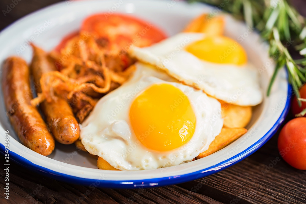 Typial breakfast with eggs, tomato, onion rings and sausage on plate Typial breakfast with eggs, tomato, onion rings and sausage on plate