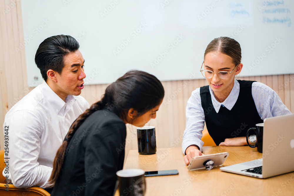 A good looking, confident and fit Asian Chinese man is speaking and conducting a meeting with his diverse team in a meeting room. They are looking at presentation in the smartphone A good looking, confident and fit Asian Chinese man is speaking and conducting a meeting with his diverse team in a meeting room. They are looking at presentation in the smartphone