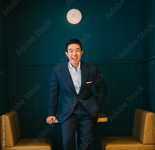 Fotografía A young, attractive and masculine professional Chinese Asian businessman leaning against a table as he laugh to his colleague whose out of view
