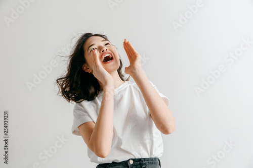 Do not miss. Young casual woman shouting. Shout. Crying emotional woman screaming ongray studio background. Female half-length portrait. Human emotions, facial expression concept. photo