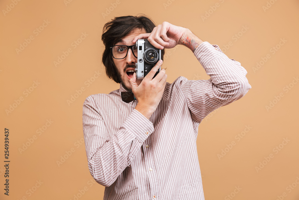 Image of intelligent man 20s wearing eyeglasses and bow tie photopraphing on retro camera while standing isolated Image of intelligent man 20s wearing eyeglasses and bow tie photopraphing on retro camera while standing isolated