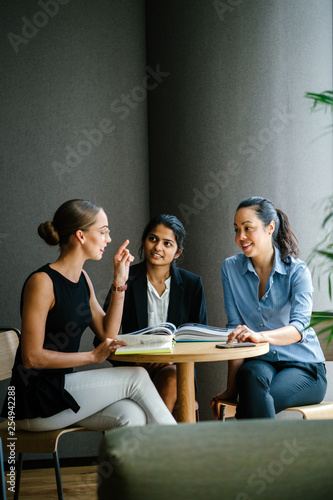 A young Caucasian woman is having a casual business meeting with her team in a meeting room. They are sitting and having an animated conversation. The team is diverse (Indian and Chinese). 