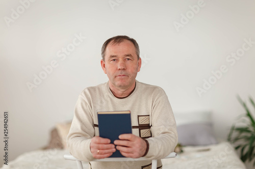 portrait of a man in a light jumper with a book on the background of a light wall and bed