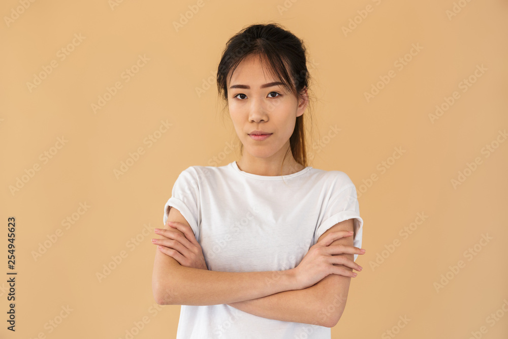 Portrait of attractive asian woman wearing basic t-shirt looking at camera while standing with arms crossed Portrait of attractive asian woman wearing basic t-shirt looking at camera while standing with arms crossed