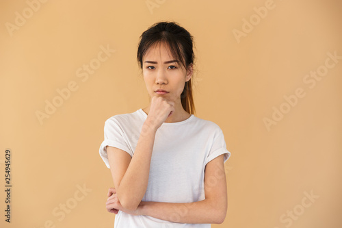 Portrait of obused asian woman wearing basic t-shirt posing at camera with angry look