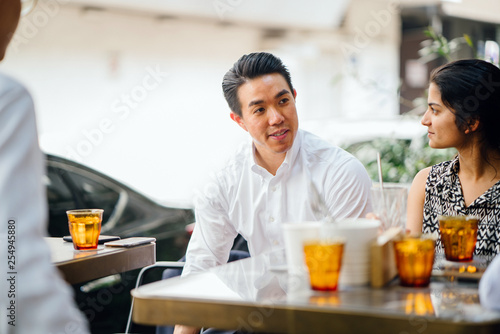 A picture of a diverse team enjoying their cocktails while sitting outdoors chatting. All of them are smiling and they seem to be having a good time.