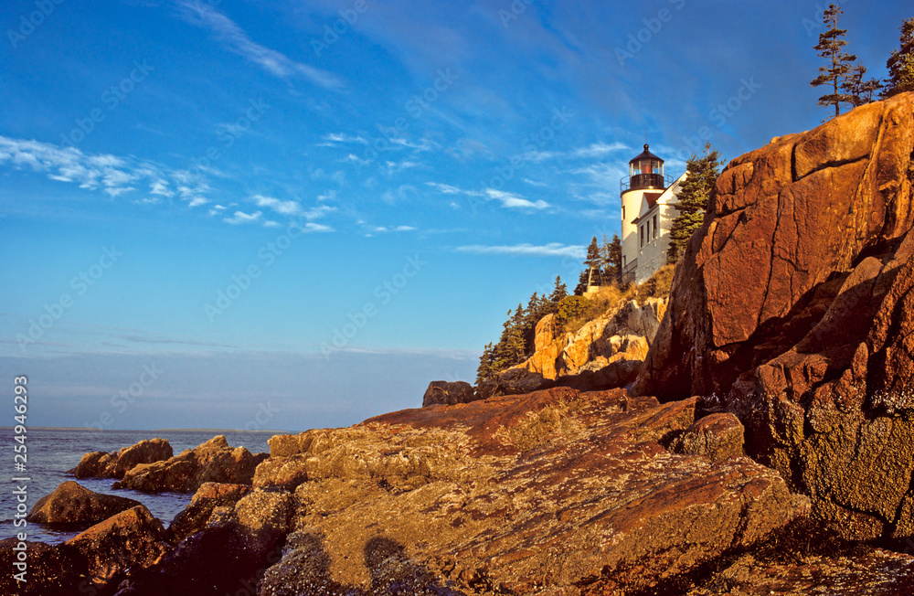 Bass Harbor Head Lighthouse catches first rays of sunrise above rocky shore on Mt. Desert Island, Maine