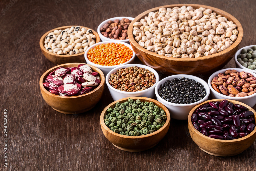 Various assortment set of indian legumes in bowls on wooden background with copyspace.