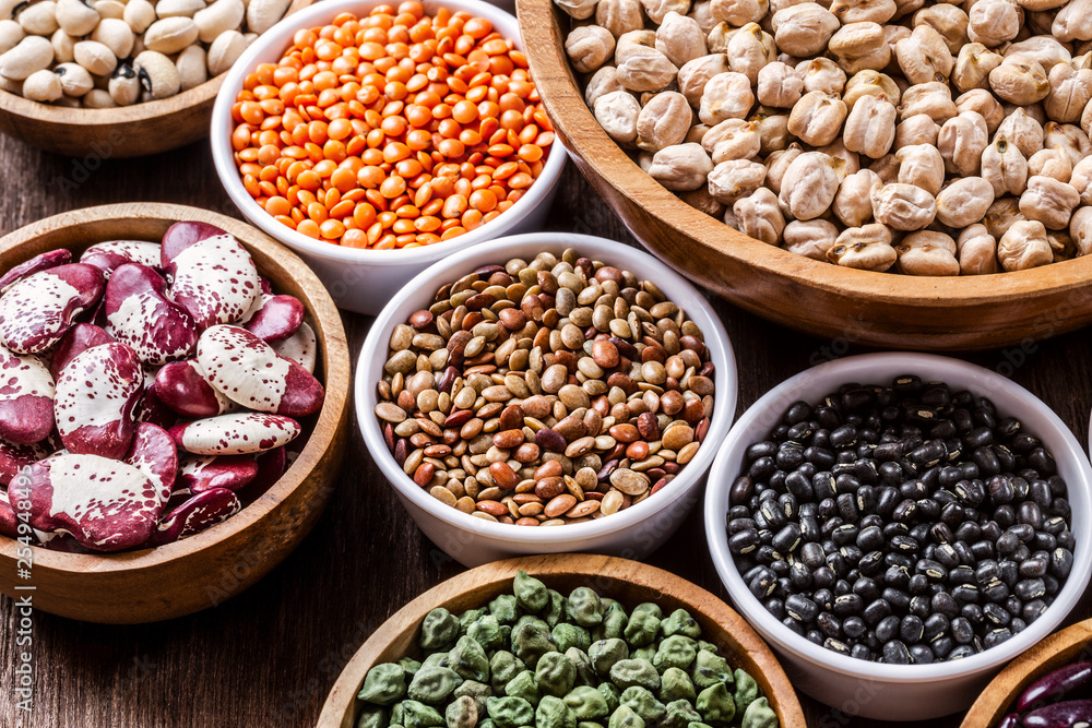 Various assortment set of indian legumes in bowls on wooden background.