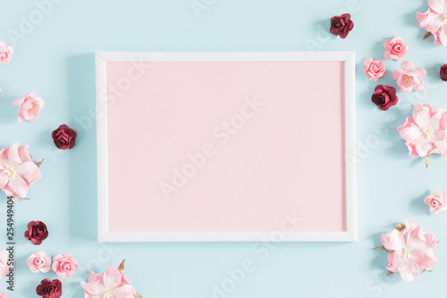 Flowers composition creative. Blank photo frame, pink flowers on pastel blue background. Flat lay, top view, copy space