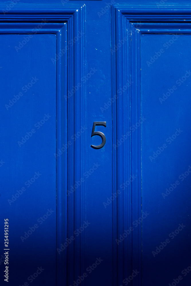 House number five in black on a bright dark blue door House number five in black on a bright dark blue door