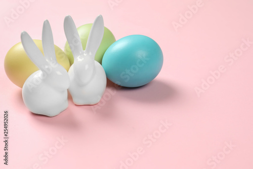 Ceramic Easter bunnies and dyed eggs on color background, space for text