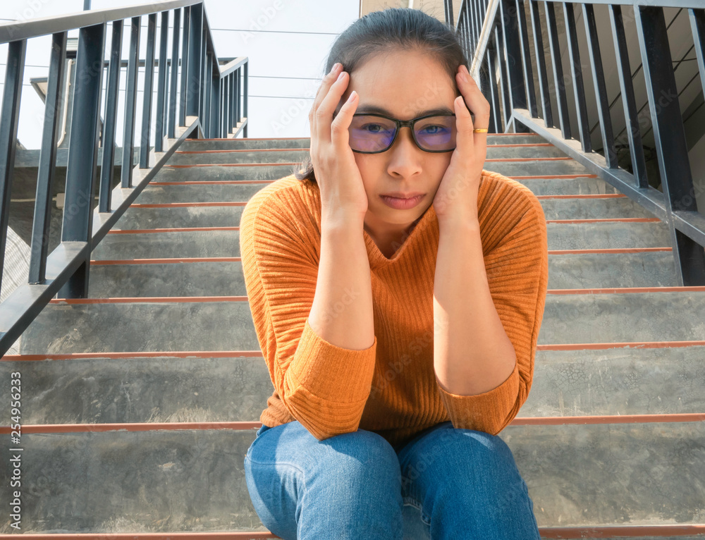 Stressed Asian woman have a headache sitting on the stairs and looking camera, woman have problem about health. Health and medical concept.