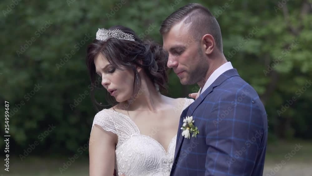 slow motion wedding couple hugs smiling and pretty bride in white lacy dress blows on open shoulder in park slow motion wedding couple hugs smiling and pretty bride in white lacy dress blows on open shoulder in park