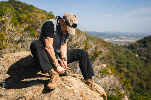 Man sitting on a rock in the nature carving a wooden stick