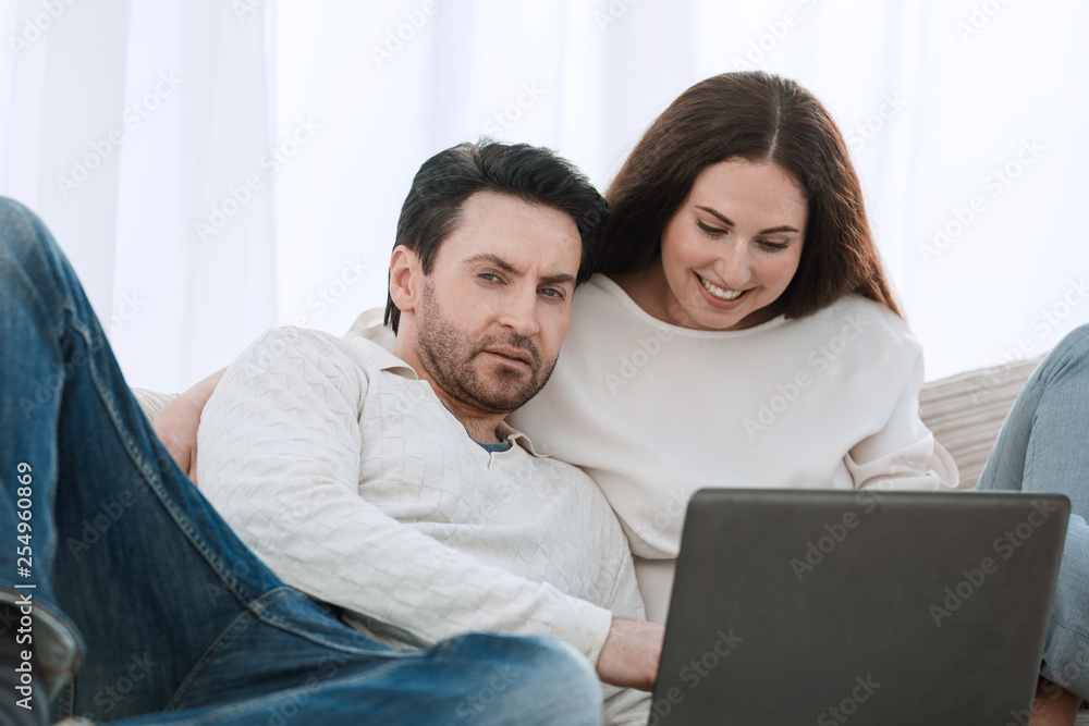 happy couple sitting on the couch in her arms, looking at laptop