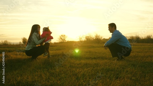 mom and dad play with kid on the grass at sunset. family happiness concept. baby goes on lawn from dad to mom. child takes first steps in park.