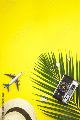 Top view traveler accessories tropical palm leaf, white straw hat, airplane toy, retro camera and seashells on yellow colorful background with space for text. Travel vacation summer concept. flat lay