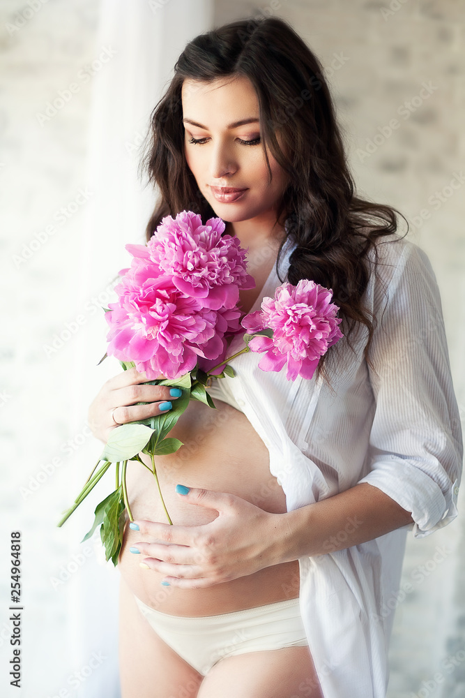 Pregnant young pretty beautiful brunette woman with pink flowers indoors