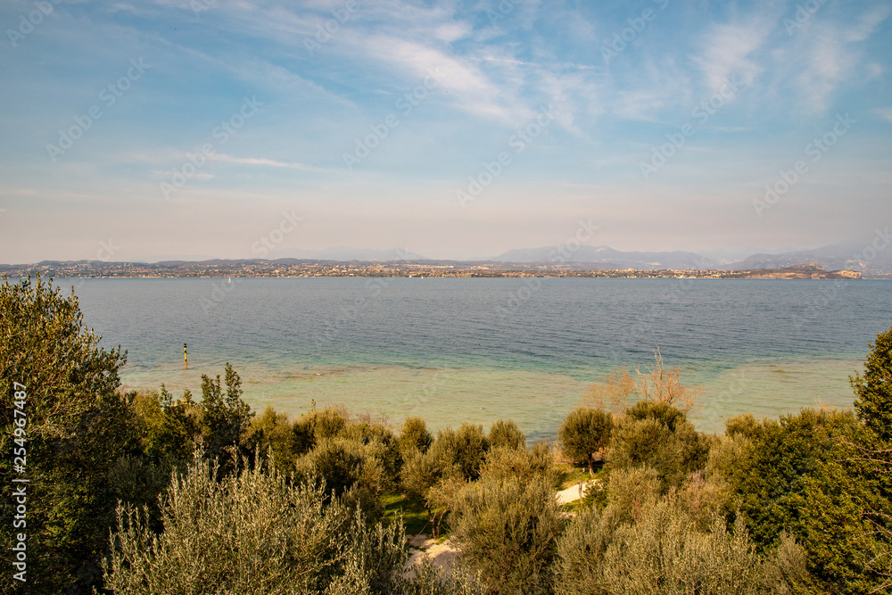 Elevated view of Lake Garda from a olive grove hill with the lake coastline on the horizon and cloudy blue sky in springtime, Sirmione, Lombardy, Italy